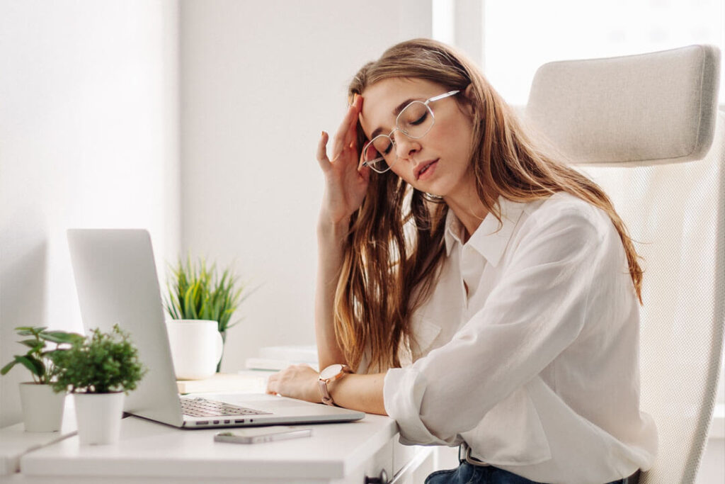Szemüveges nő a laptop előtt ülve fáradtan tartja a fejét