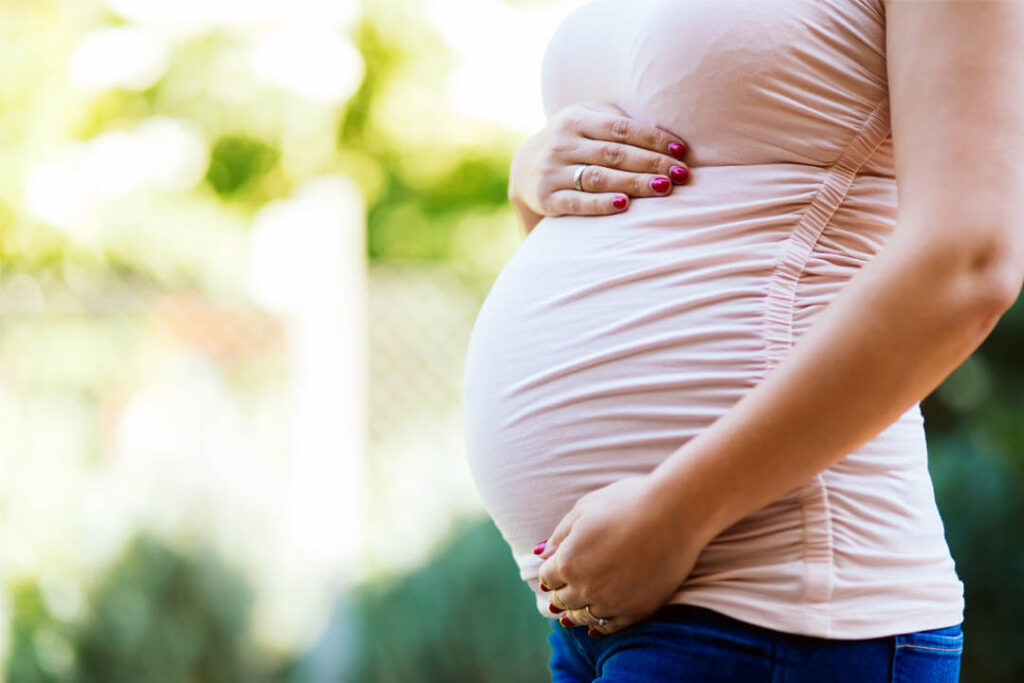Terhes nő a hasát tartja a természetes napfényben d-vitamint gyűjt