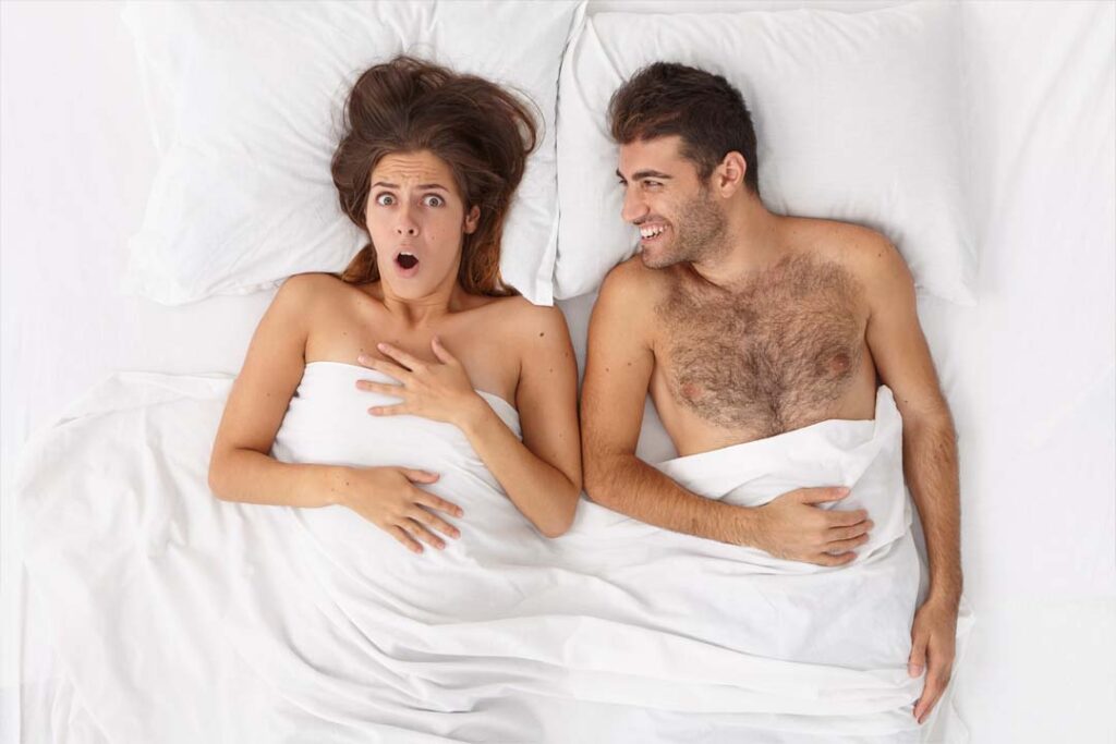 Férfi és nő egymás mellett fekszenek az ágyban fehér ágynemű között